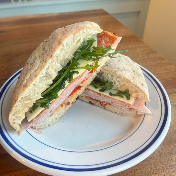 Sliced ciabatta sandwich layered with ham, salami, cheese, tomato, and arugula on a blue-rimmed plate.