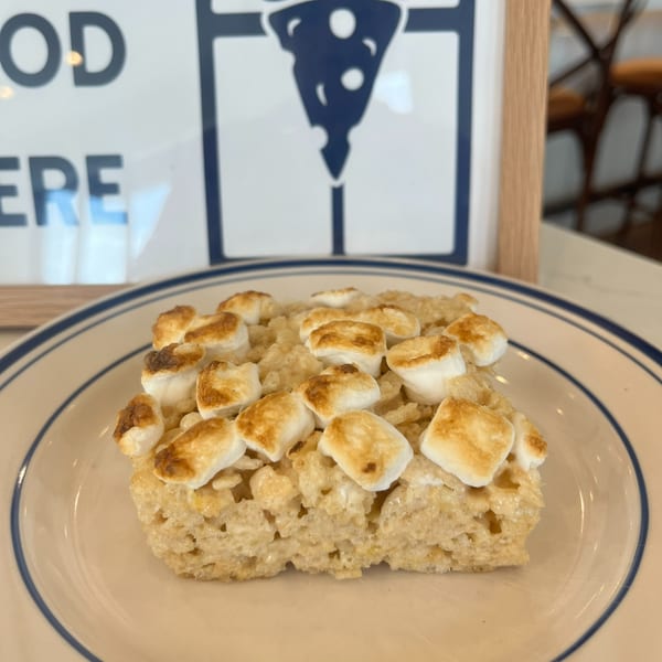 Plate of golden toasted marshmallow cereal bars displayed in front of a restaurant sign.